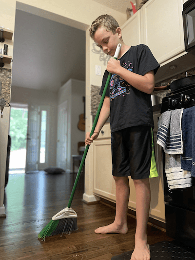 young boy doing housework by sweeping the floor
