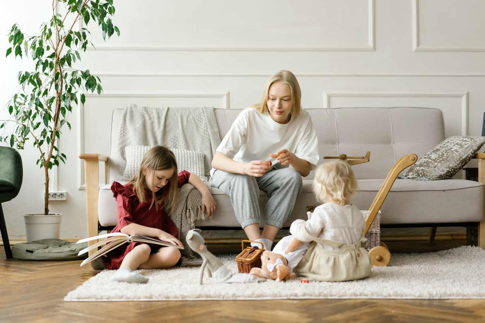 Woman in Gray Sweater Sitting on White Couch Beside Girl in White Long Sleeve Shirt