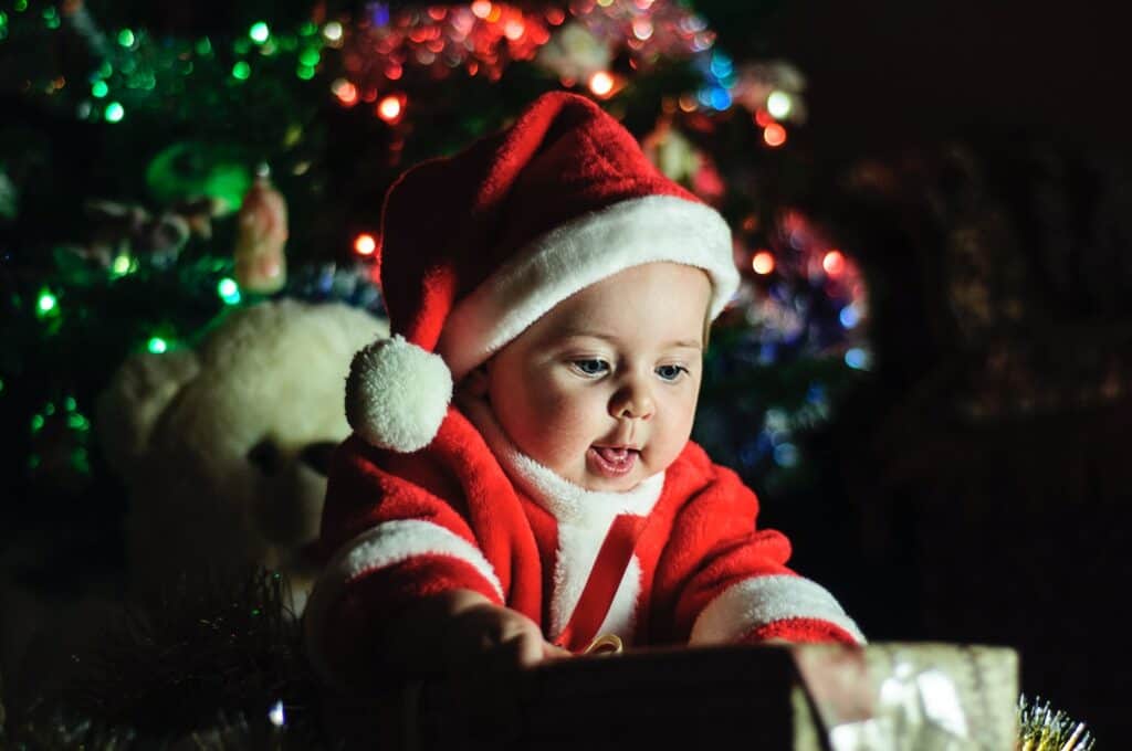 baby wearing Santa Claus outfit near Christmas tree fun holiday tradition