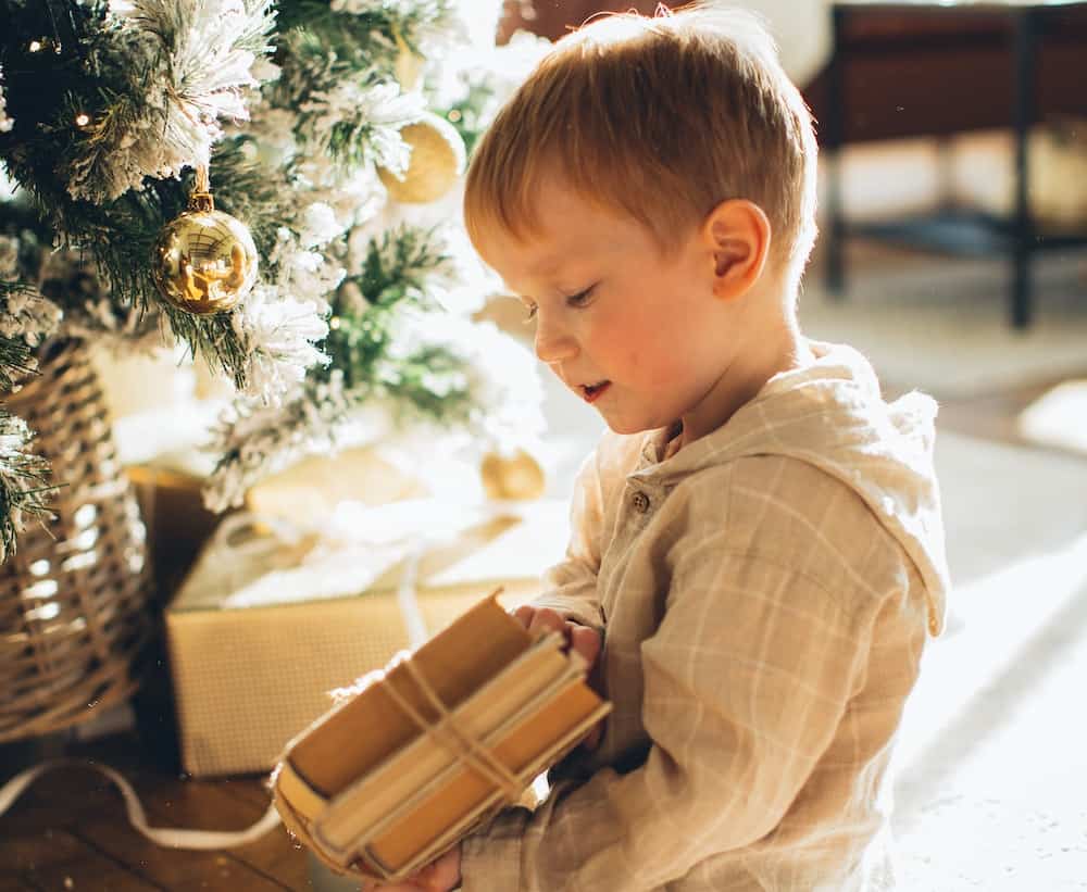 boy by a christmas tree with books in his hands