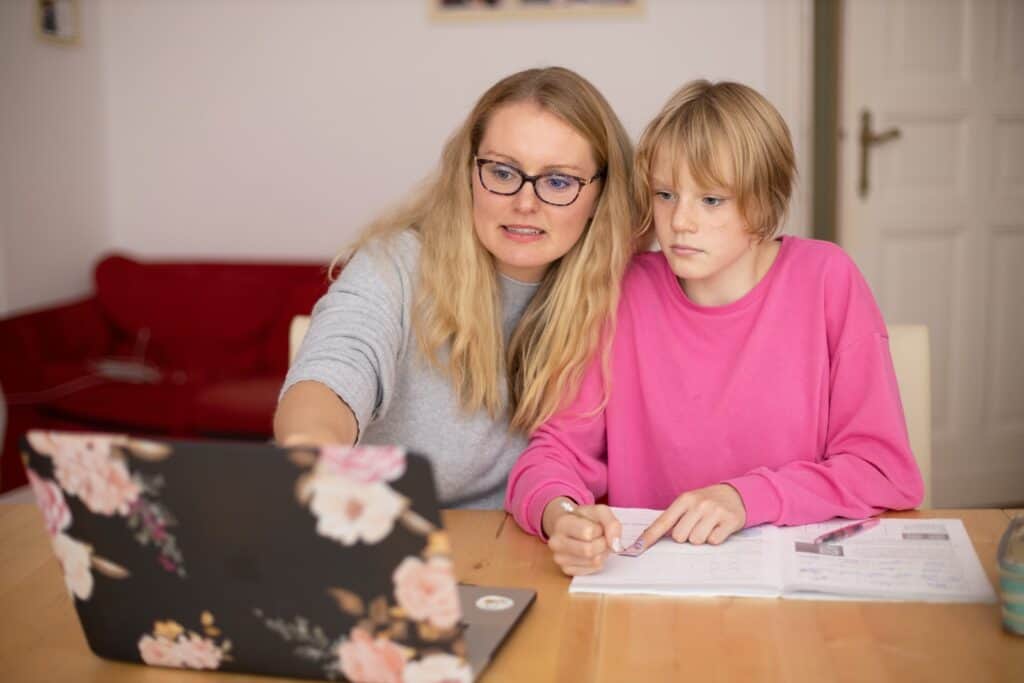 girl in pink sweater beside mom in gray sweater. looking at computer