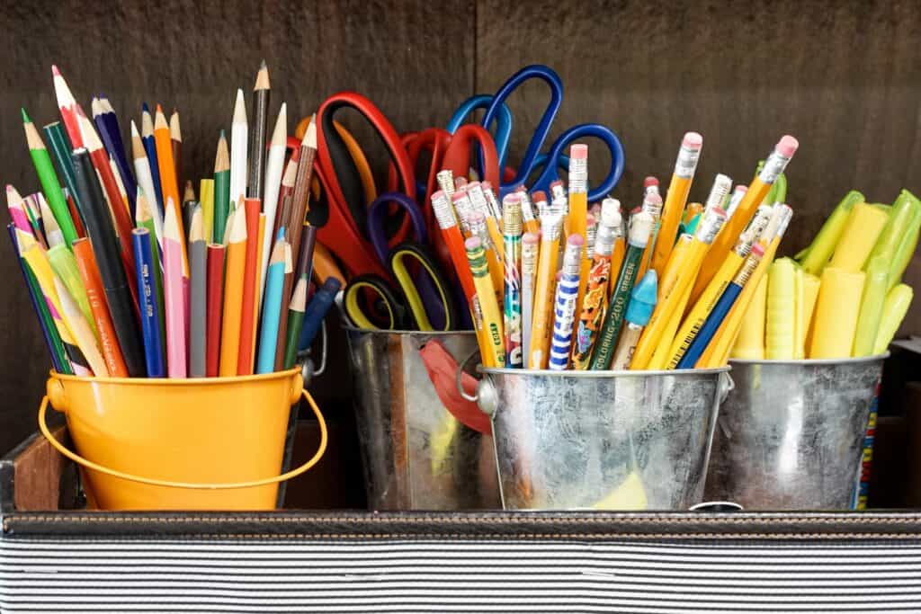 homeschool supplies organized into small buckets by type. Colored pencils, pencils, markers, scissors. 