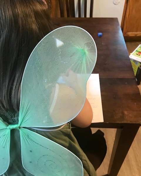girl doing homeschool work while wearing fairy wings, making her curriculum work more fun