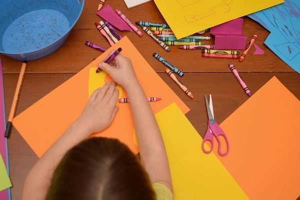 child coloring on construction paper with colorful crayons