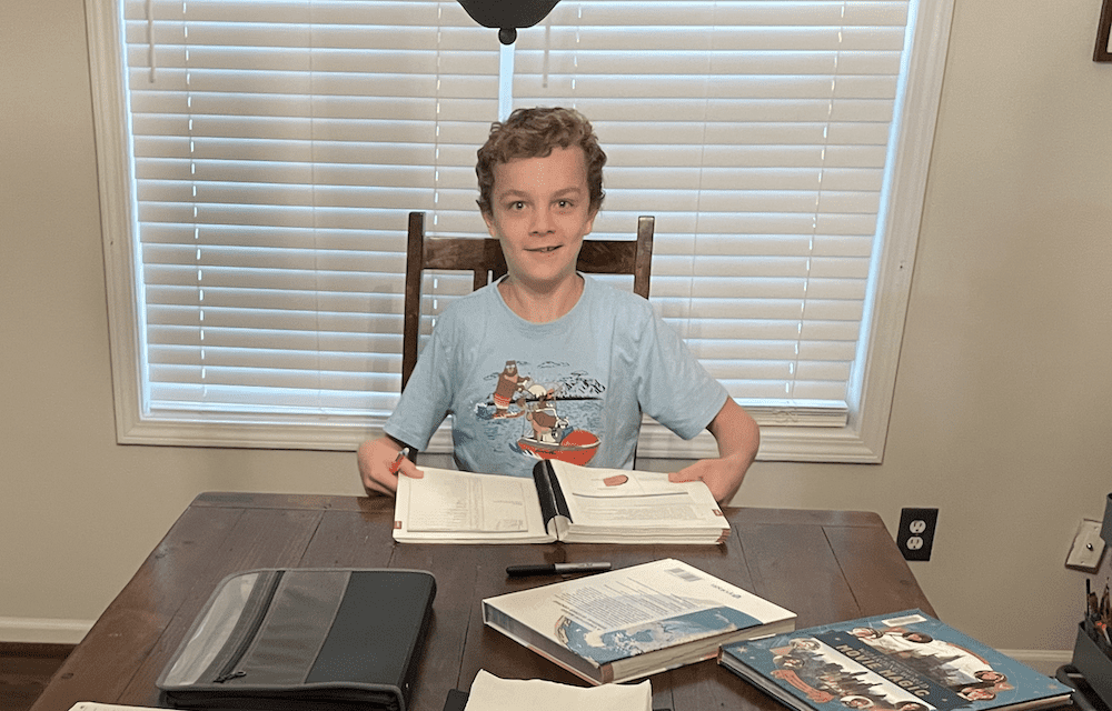 boy reluctantly smiling holding homeschool curriculum