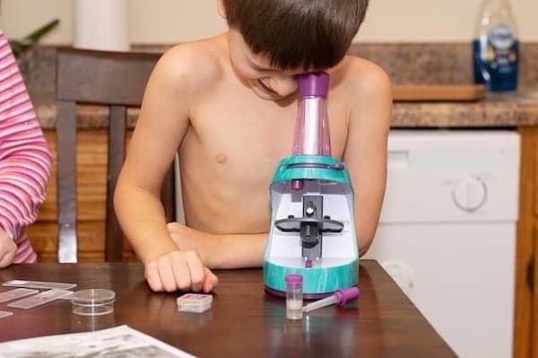 kindergarten homeschool boy without shirt looking into microscope