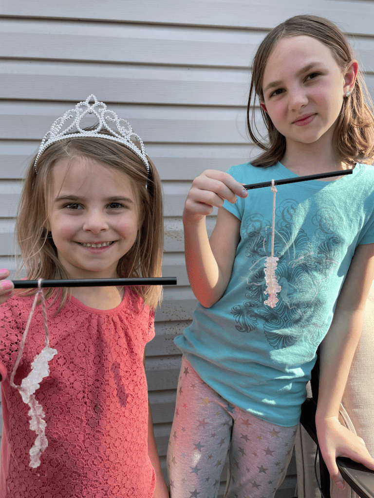 two girls holding pencils with hanging rock candy for a kinderarten homeschool science curriculum experiment