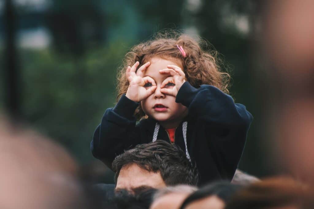 little girl looking through her fingers like they're glasses 
