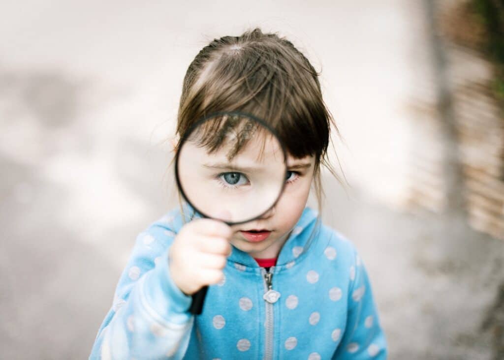 girl in blue and white polka dot jacket looking through a magnifying glass at you