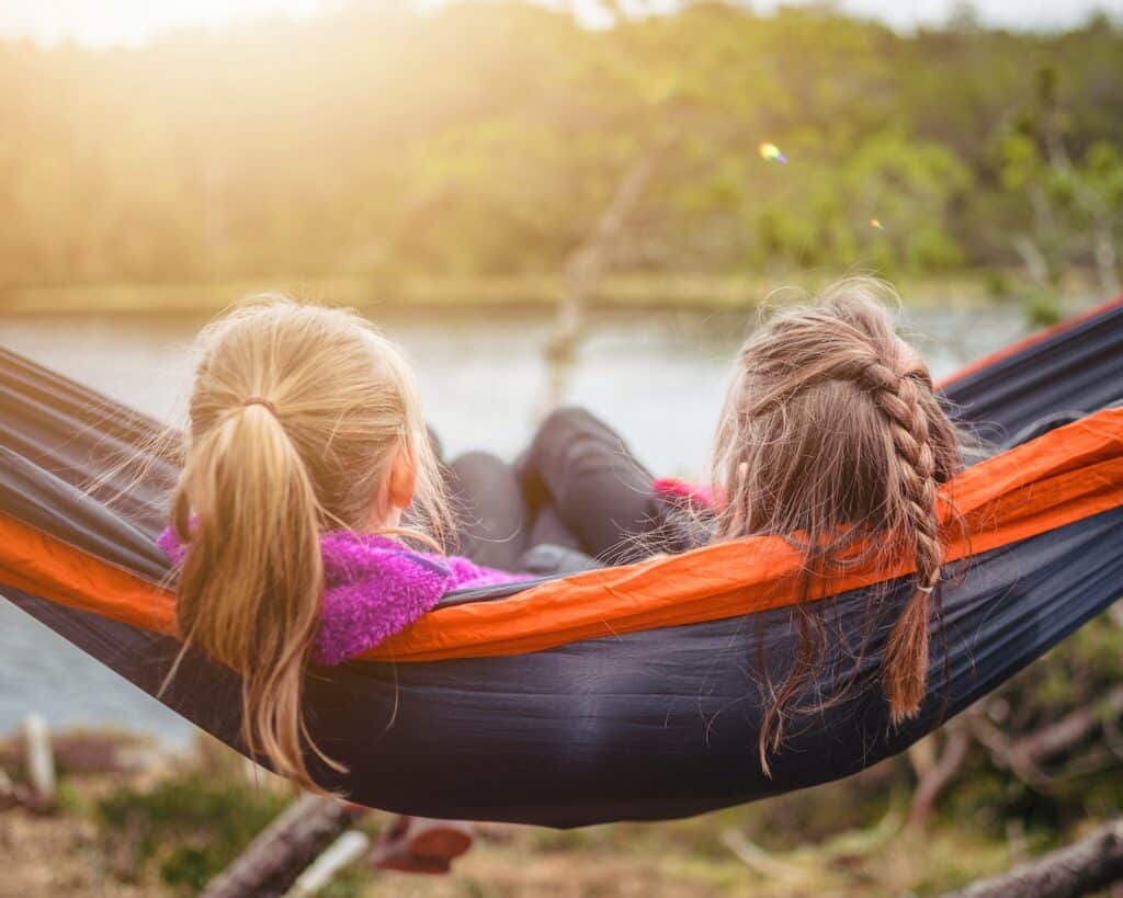two girls lying on hammock looking at the lake