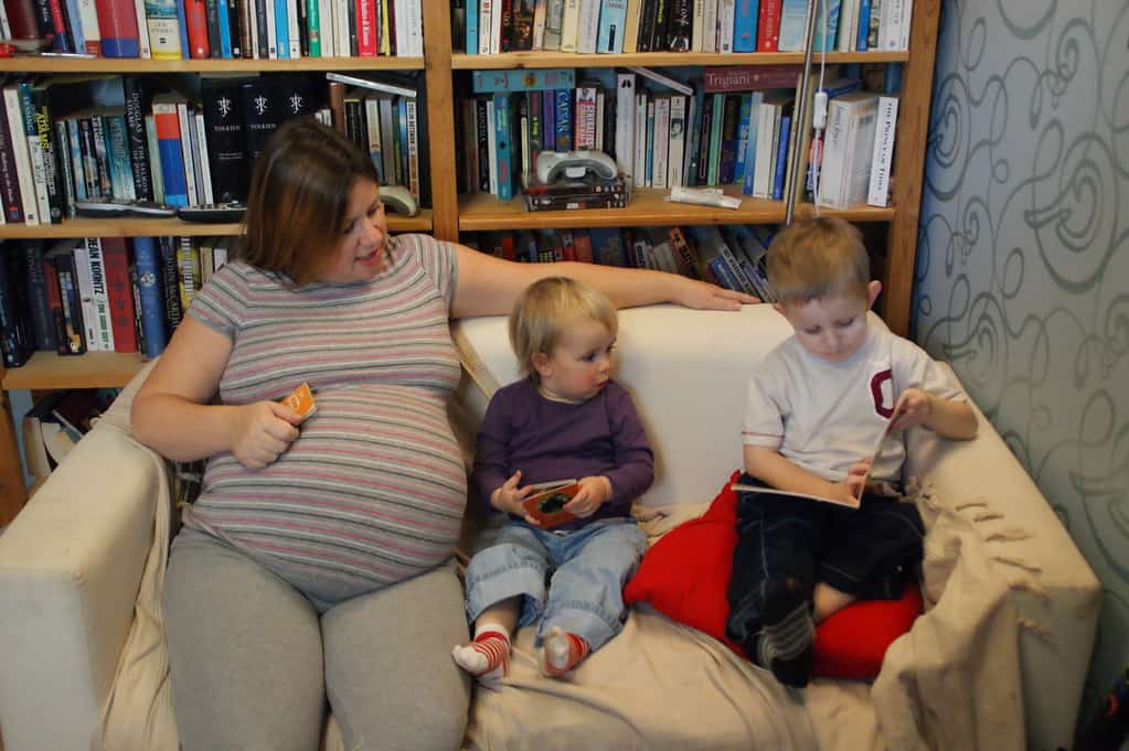 Pregnant mama on couch with two small kids reading books together