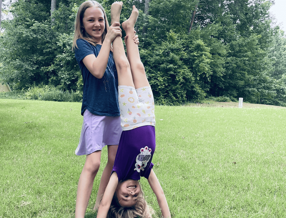 a young girl doing a handstand while another girl holds her legs