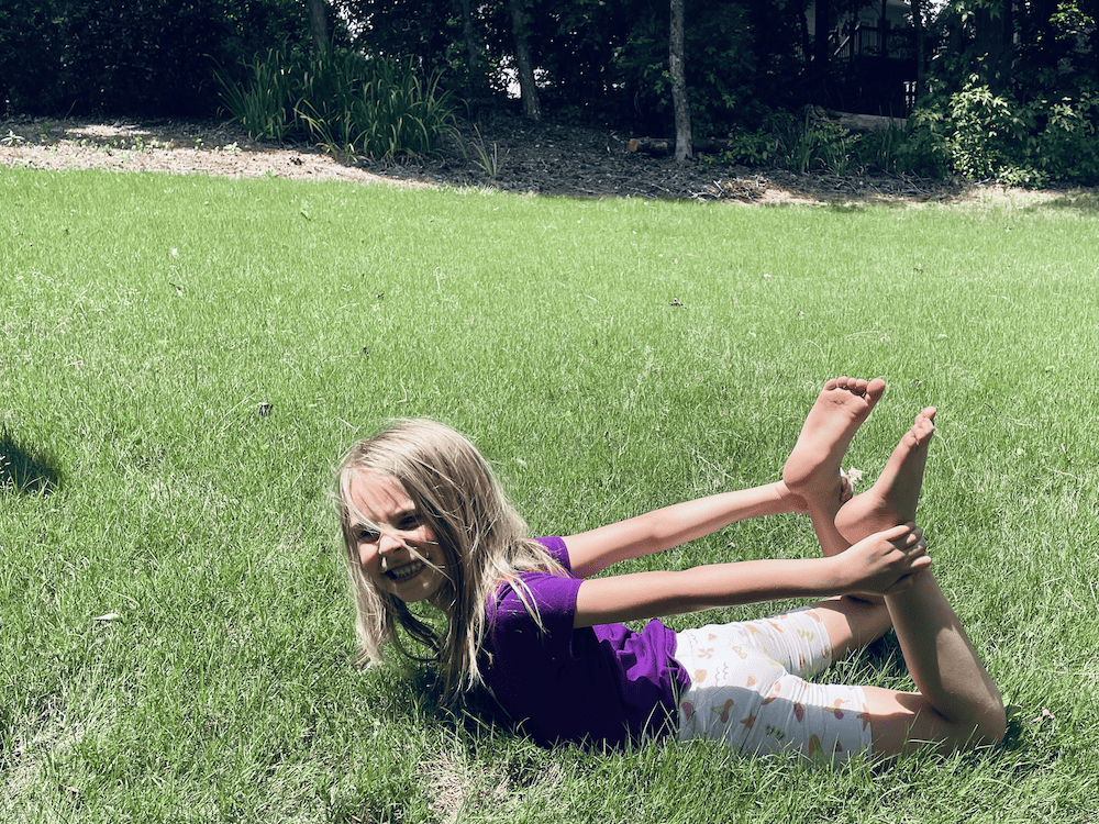 a young girl holding her ankles in the grass