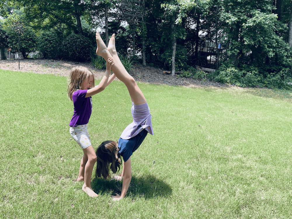 a young girl doing a handstand while another girl holds her legs