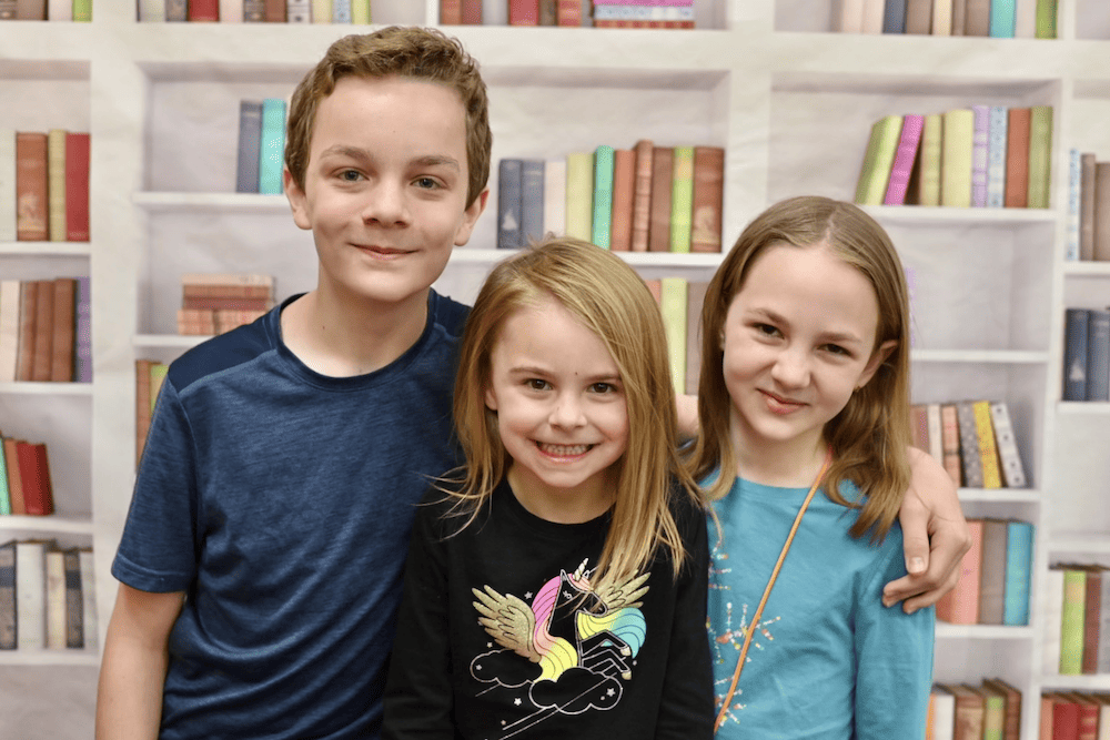 3 kids smiling with books in the background