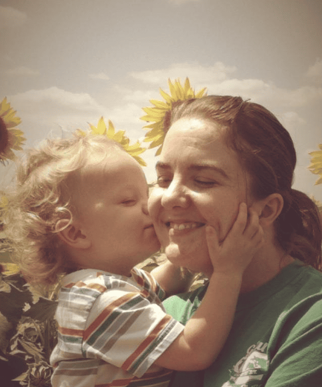 a toddler kissing his mom's cheek with sunflowers in the background