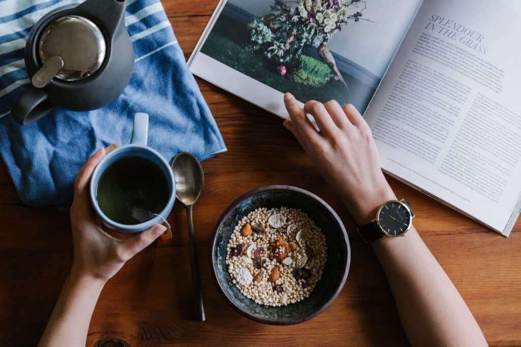 person holding blue ceramic mug and white magazine. scheduls and routines