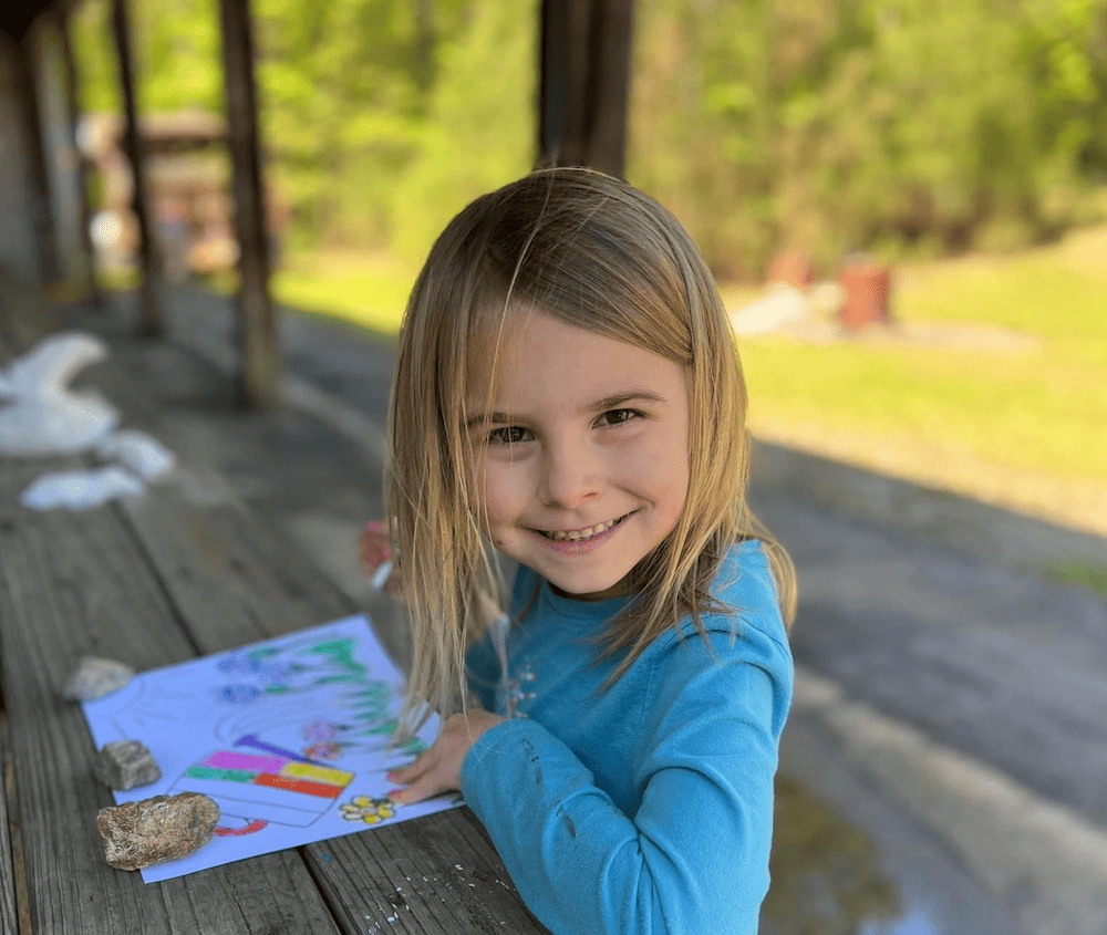 young girl coloring outside and smiling