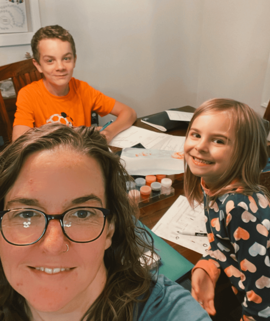 mom and two kids smiling doing schoolwork together