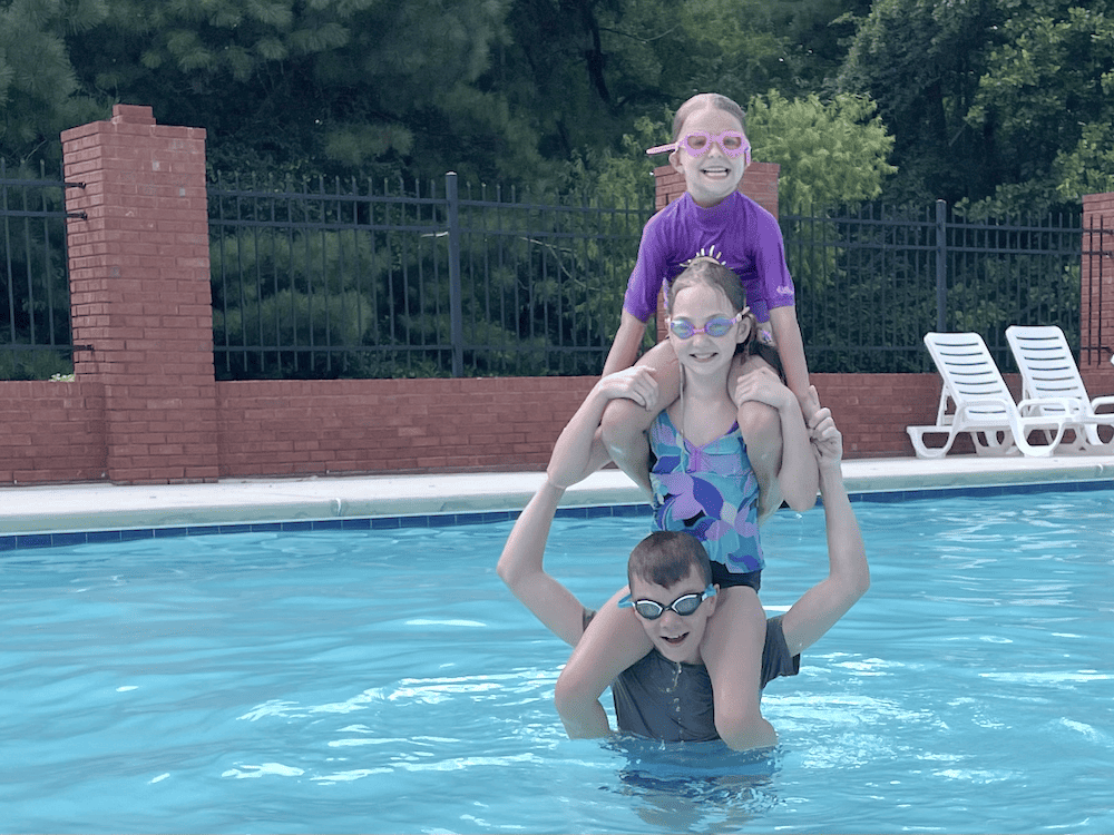 3 kids on shoulders in a pool. skipping a school day