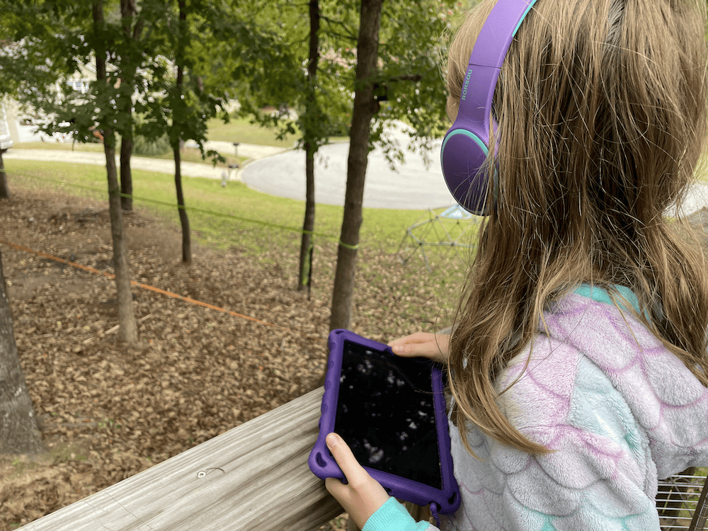 girl looking at trees while listening to audiobook on headphones