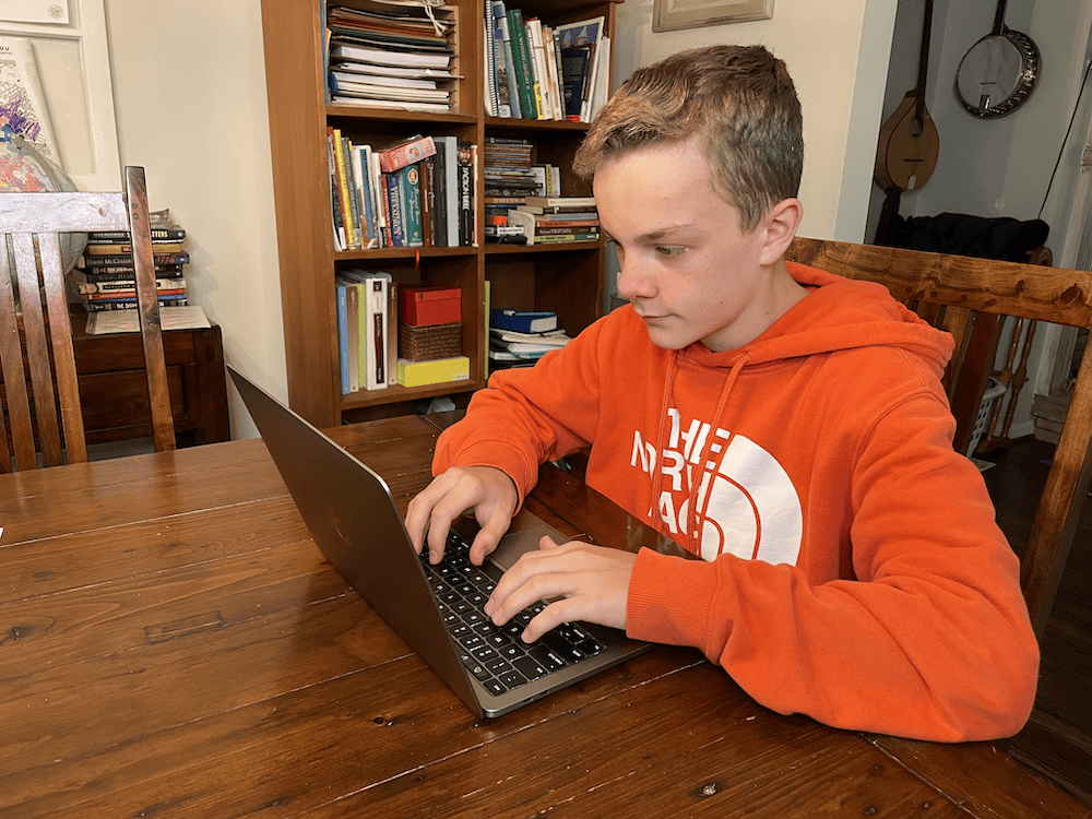 boy in orange sweatshirt typing on a computer