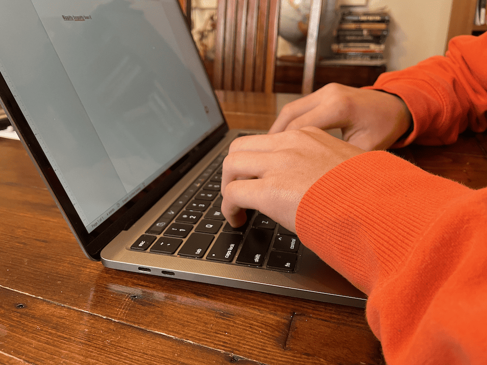 hands with orange sleeves typing on a computer
